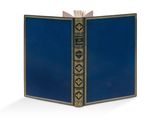 un livre bleu ouvert, aux bords dorés, posé sur une surface blanche