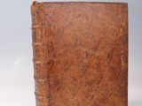 an old brown book sitting on top of a table next to a white wall