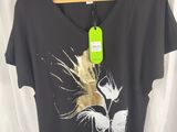Le t-shirt est noir et orné d'une fleur dorée.