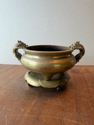 a small bronze bowl on a wooden table with a white wall in the background