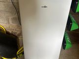 a small white refrigerator in the corner of a room next to a pile of books