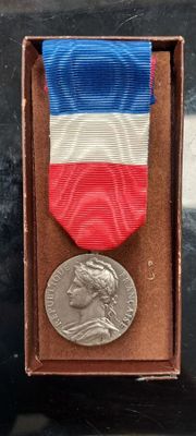 une médaille d'argent dans une boîte ornée d'un ruban rouge, blanc et bleu