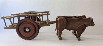 a wooden toy of a cow pulling a cart with a cow