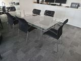 une table en verre avec des chaises noires et une télévision accrochée au mur