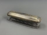 une vieille boîte en argent avec un couvercle, posée sur une surface grise