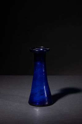 blue glass vase sitting on a table in a dark room
