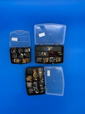 trois boîtes contenant différents types de bijoux, posées sur un fond bleu