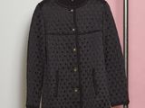 une veste noire accrochée à un porte-vêtements devant un mur rose et blanc