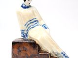 a figurine of a woman sitting on a piece of wood