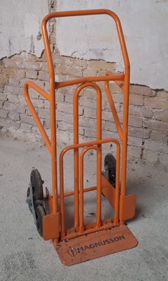 an orange hand truck with wheels in front of a brick wall