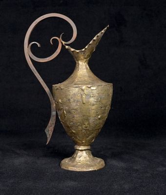 a gold vase with a curved handle on a black background