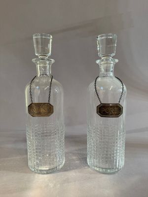 pair of clear glass bottles with a gold label and a chain around the neck