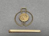 a close up of a gold tie bar with a coin on it