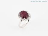 a close up of a ring with a red stone surrounded by diamonds