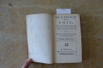 un livre ouvert posé sur une table, à côté de la main d'une personne