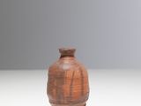 un petit vase brun posé sur une surface blanche