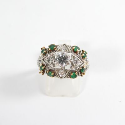 a close up of a diamond and emerald ring on a white surface