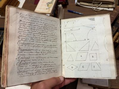 quelqu'un tient un livre sur lequel figure un dessin, devant une pile de livres