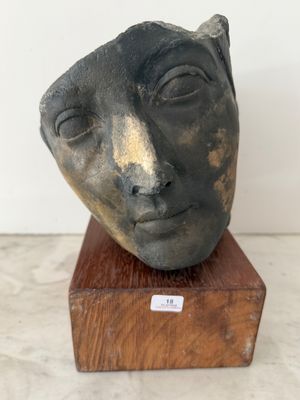 une photo d'une sculpture représentant le visage d'un homme, posée sur un socle en bois