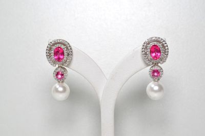 une paire de boucles d'oreilles en perles roses et blanches posées sur un présentoir blanc