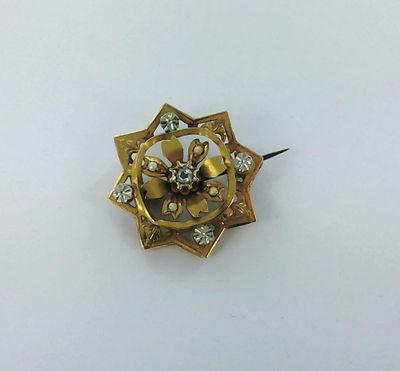 a close up of a gold and diamond broochle on a white surface