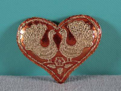 a red and gold heart shaped brooch with two birds on it