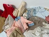 a pile of baby clothes on a bed next to a pillow