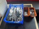 un panier contenant des couverts posé sur une table à côté d'un récipient contenant des couverts