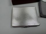 a silver cigarette case sitting on a table next to a wallet