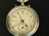 une petite montre de poche en argent posée sur une surface noire