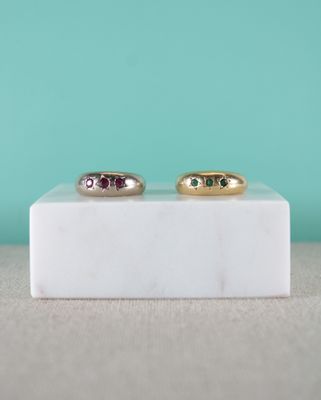 une paire de bagues en or ornées de pierres vertes et roses, posées sur un bloc de marbre