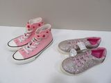 Deux paires de Converse roses et argentées sont posées sur une surface blanche.