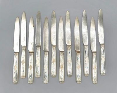 six silverplated knives are lined up in a row on a gray surface