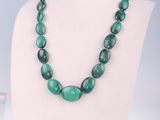 a close up of a necklace with green beads on a mannequin