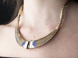 La femme porte un haut noir et un collier doré et bleu.