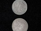 two silver coins sitting side by side on a black surface