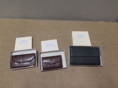 quatre modèles différents de portefeuilles en cuir, rangés dans une boîte posée sur une table