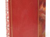 an old red book with gold trim sitting on top of a white surface