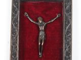 crucifix en métal argenté posé sur du velours rouge, dans un cadre ouvragé
