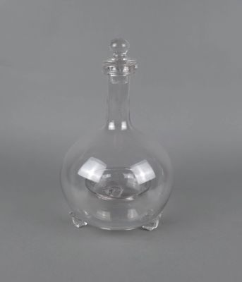 une carafe en verre transparent avec un socle en métal, sur fond gris