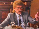 un homme en costume-cravate, assis à une table devant une assiette de nourriture