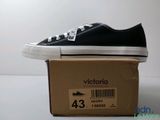 Des Converse noires et blanches sont posées sur une boîte en carton posée sur une surface blanche