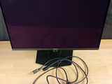 un écran d'ordinateur posé sur un bureau en bois, à côté d'un chargeur