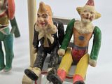 three figurines of clowns sitting on a bench