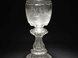 un gobelet en verre posé sur un socle, sur fond noir