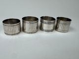 four silver napkin rings with designs on them on a white surface