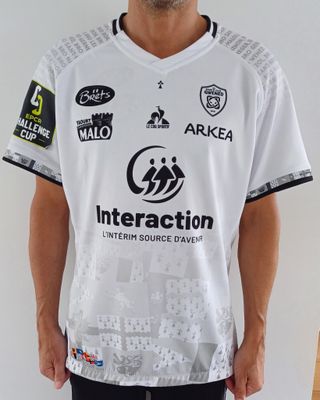 un homme debout devant un mur blanc, vêtu d'une chemise blanche