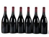 six bottles of red wine lined up in a row on a white surface