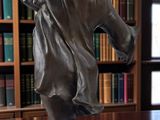 a statue of a boy standing on a table in front of a bookshelf