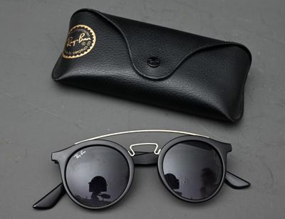 des lunettes de soleil noires et un étui noir posés sur une table, à côté d'une autre paire de lunettes de soleil